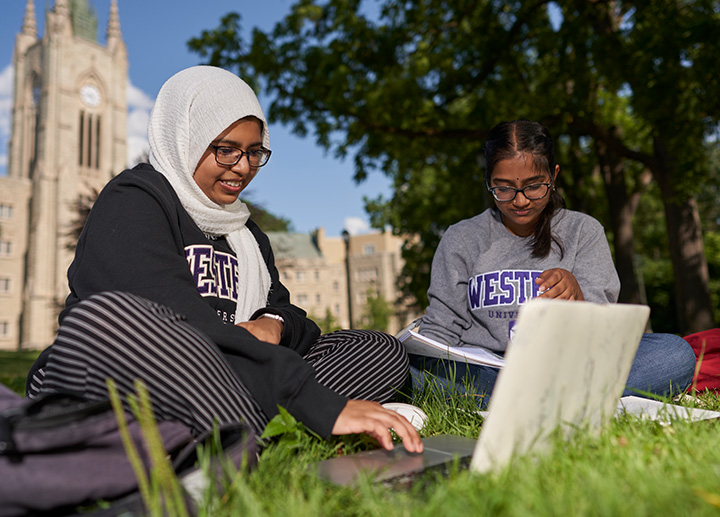 Two girls sitting down outside and doing homework